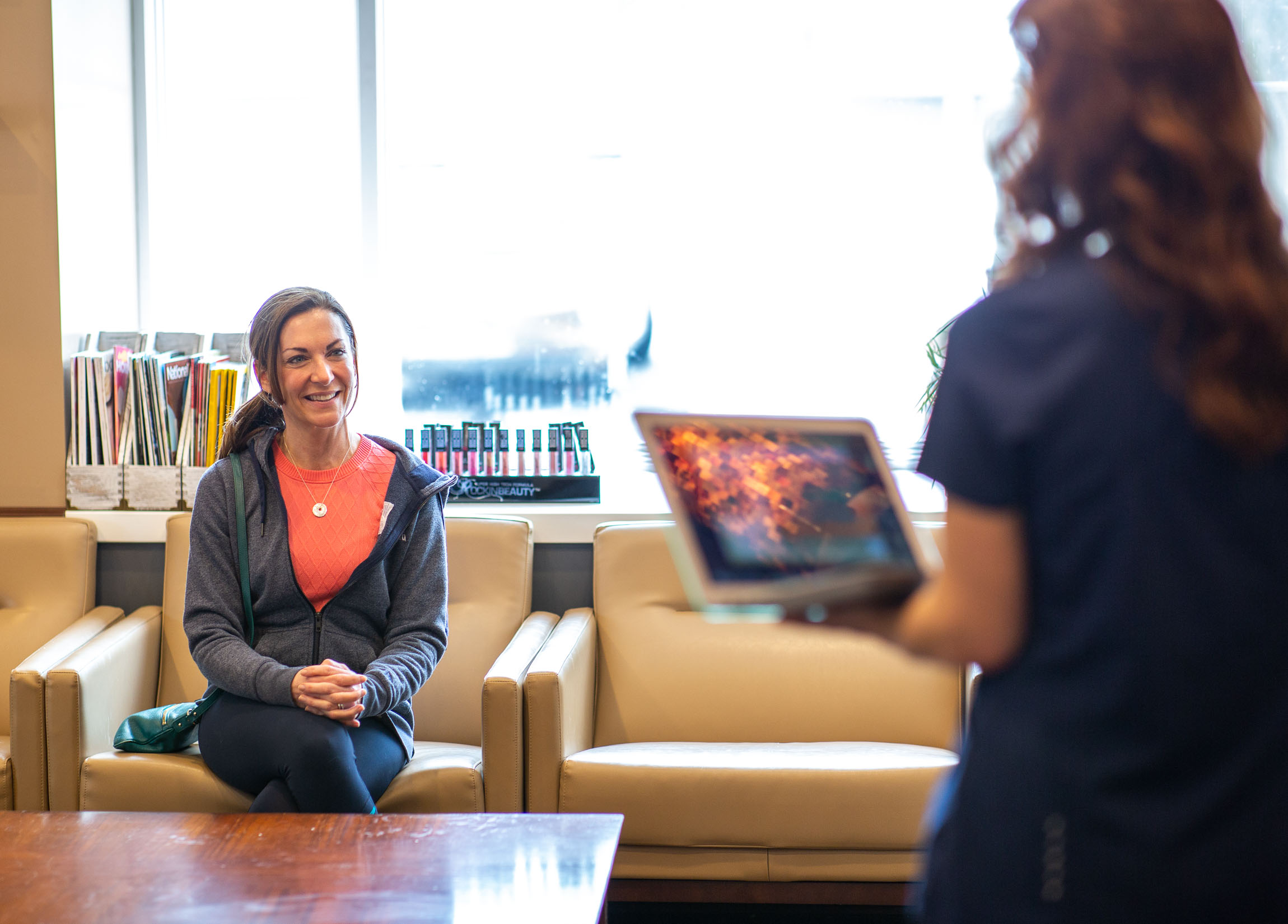 A patient meets with a specialist holding a laptop before her Hydrafacial.